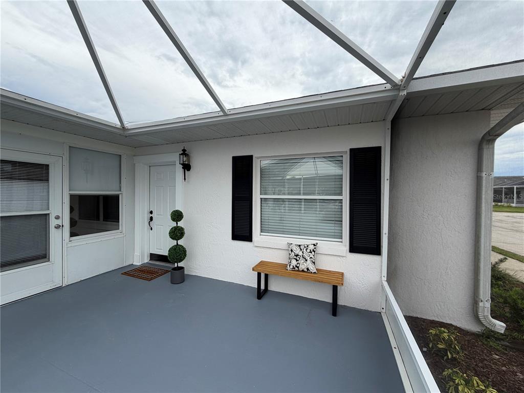 A covered patio features a white door, a wooden bench, and a gray painted floor — 2947 TANGERINE COURT, LEESBURG, FL