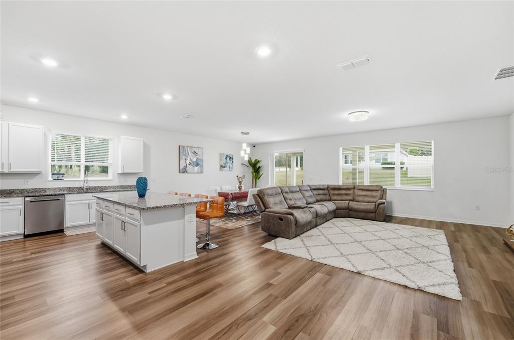 An open-concept kitchen, dining area, and living room with wood-look flooring and a large sectional — 2081 MALBEC COURT, MINNEOLA, FL