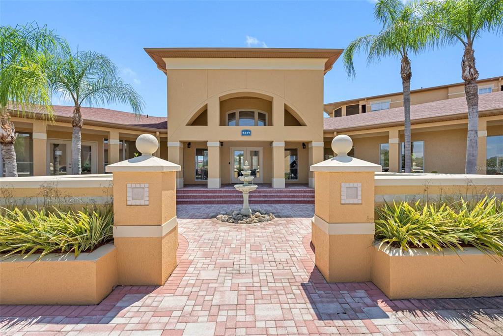 The exterior of a tan building features a paved walkway, a central fountain, and palm trees — 4323 BAYSIDE VILLAGE DRIVE UNIT 329, TAMPA, FL