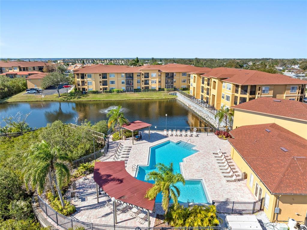 An aerial view shows a swimming pool, a gazebo, and apartment buildings beside a pond — 4323 BAYSIDE VILLAGE DRIVE UNIT 329, TAMPA, FL