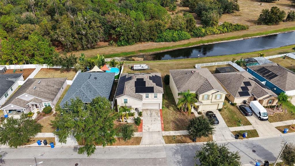 An aerial view shows a row of suburban houses with solar panels and backyards facing a canal — 10657 STANDING STONE DR, WIMAUMA, FL