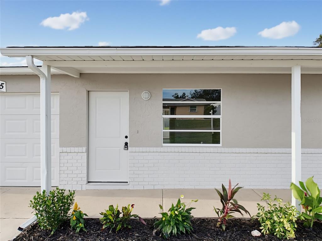 A view of a house exterior featuring a white door, window, and front garden — 2245 BISHOP ROAD, SPRING HILL, FL