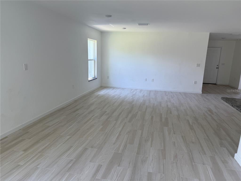 An empty room features light-colored wood-look tile flooring, white walls, and a single window — 2408 VAN LEER AVENUE, NORTH PORT, FL
