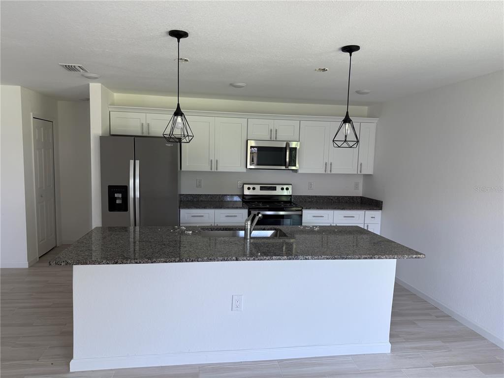 A kitchen features white cabinets, granite countertops, stainless steel appliances, and a large center island — 2408 VAN LEER AVENUE, NORTH PORT, FL