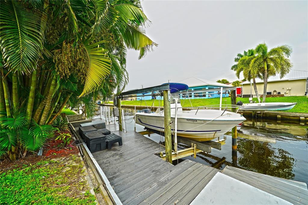 A white boat sits on a lift at a wooden dock beside a canal — 7228 REYMOOR DRIVE, NORTH FORT MYERS, FL