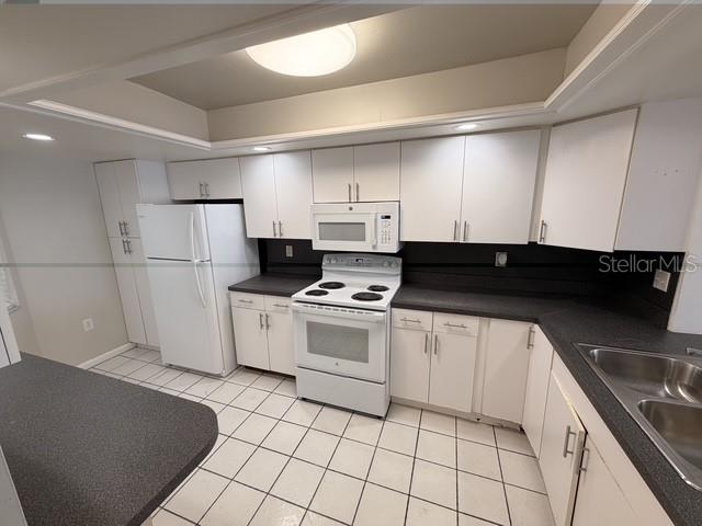 A kitchen features white cabinets, dark countertops, white appliances, and white tiled flooring — 4109 FAIRVIEW VISTA POINT UNIT 315, ORLANDO, FL