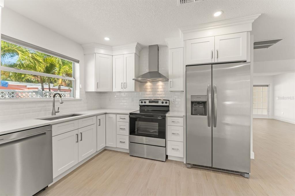 A modern kitchen features white cabinets, stainless steel appliances, and light wood-look flooring — 107 4TH STREET, BELLEAIR BEACH, FL