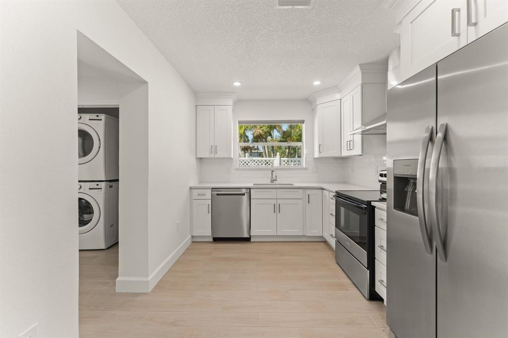 A kitchen with white cabinets, stainless steel appliances, and a laundry area to the left — 107 4TH STREET, BELLEAIR BEACH, FL