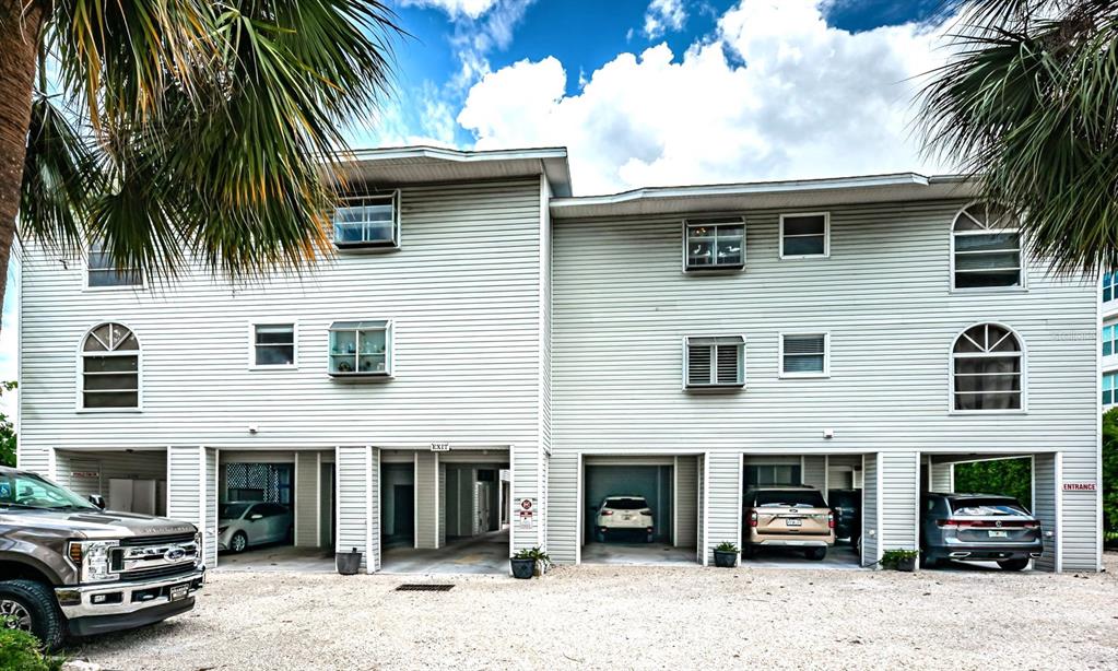 A three-story building with light-colored siding features covered parking bays on the ground level — 20019 GULF BOULEVARD UNIT 9, INDIAN SHORES, FL