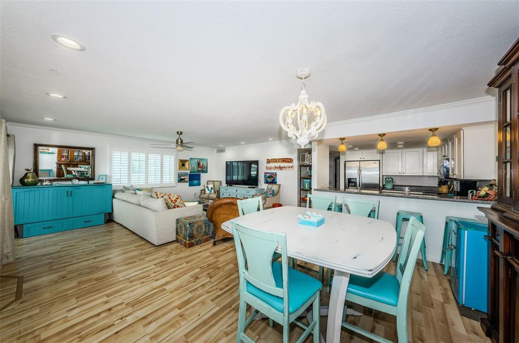 An open-concept living and dining area features light wood floors, turquoise furniture, and a chandelier — 20019 GULF BOULEVARD UNIT 9, INDIAN SHORES, FL