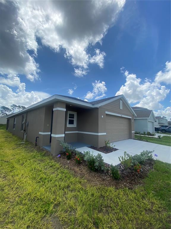 A tan, single-story house with a two-car garage and a small landscaped front yard — 11511 MEMORIAL DRIVE, BROOKSVILLE, FL