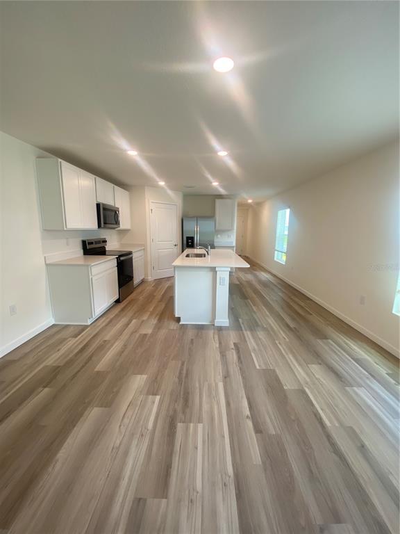 A kitchen features white cabinets, a central island, stainless steel appliances, and light wood flooring — 11511 MEMORIAL DRIVE, BROOKSVILLE, FL
