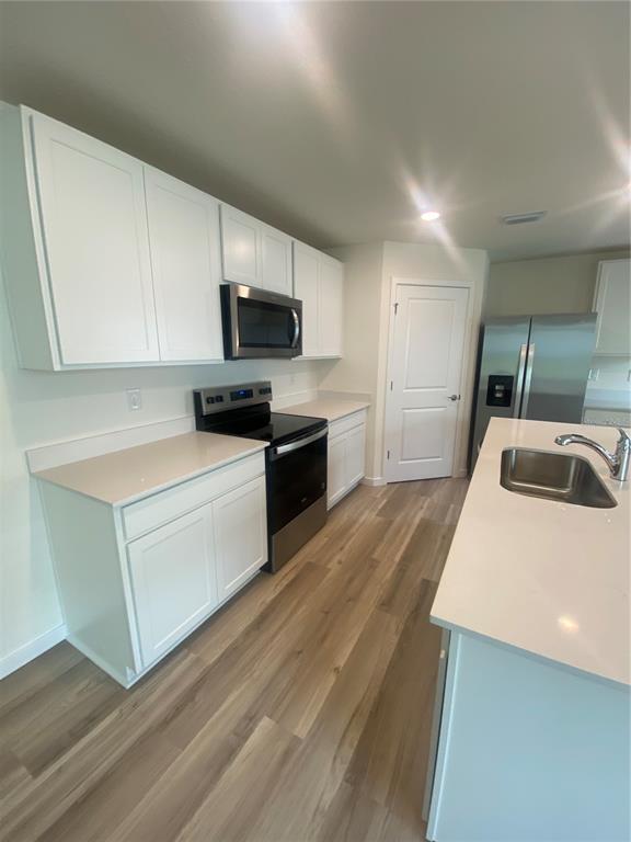 A kitchen features white cabinets, stainless steel appliances, quartz countertops, and light wood-look flooring — 11511 MEMORIAL DRIVE, BROOKSVILLE, FL