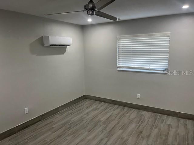 A bedroom features light gray walls, wood-look tile flooring, a ceiling fan, and a wall-mounted AC — 1605 PASS A GRILLE WAY UNIT 2, ST PETE BEACH, FL