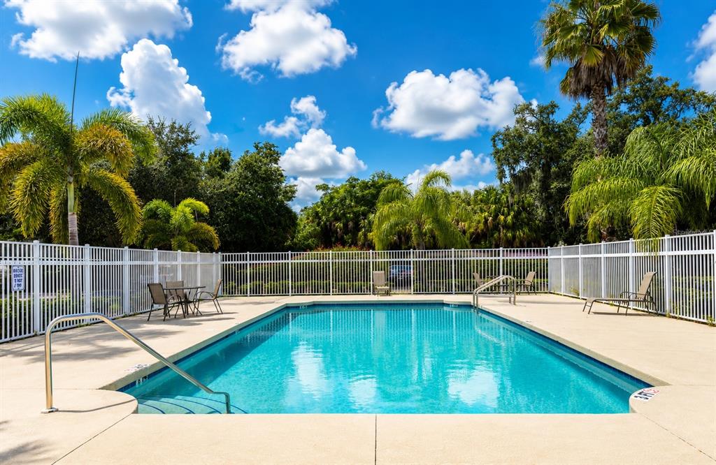 A rectangular swimming pool is surrounded by a white fence, patio furniture, and palm trees — 2607 RIVER PRESERVE COURT UNIT 2607, BRADENTON, FL