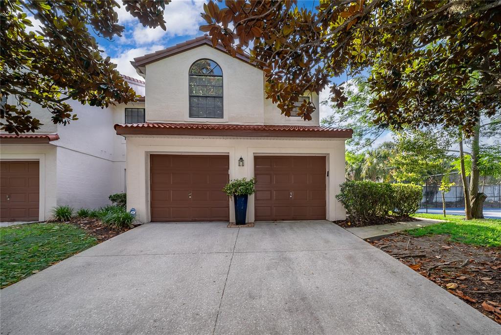 A two-story townhouse exterior features a two-car garage, a concrete driveway, and arched windows — 520 VIA VERONA LANE UNIT 203, ALTAMONTE SPRINGS, FL