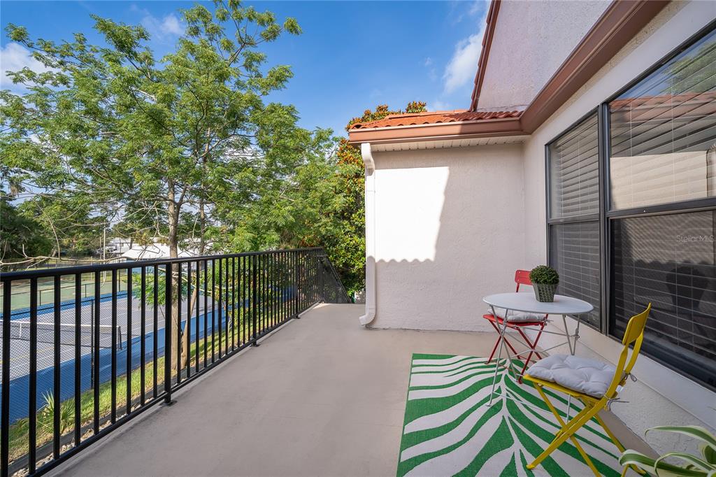 A balcony with a metal railing overlooks a tennis court next to a building exterior — 520 VIA VERONA LANE UNIT 203, ALTAMONTE SPRINGS, FL