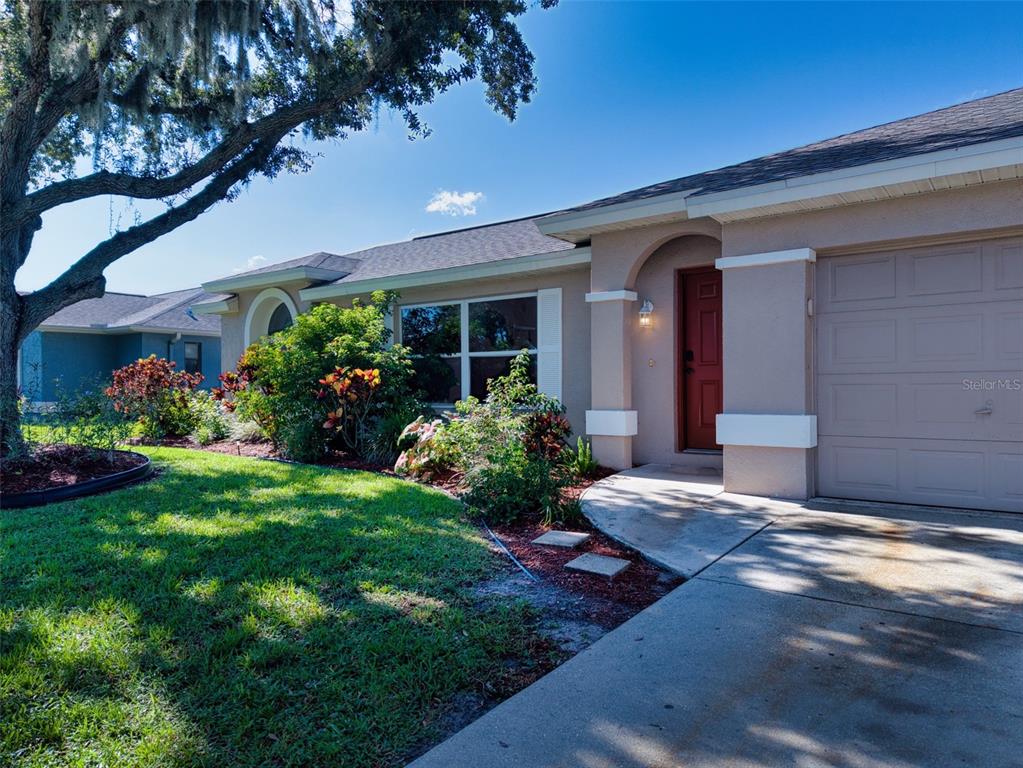 A tan house exterior features a red front door, a garage, and a landscaped yard — 6305 61ST STREET E, PALMETTO, FL