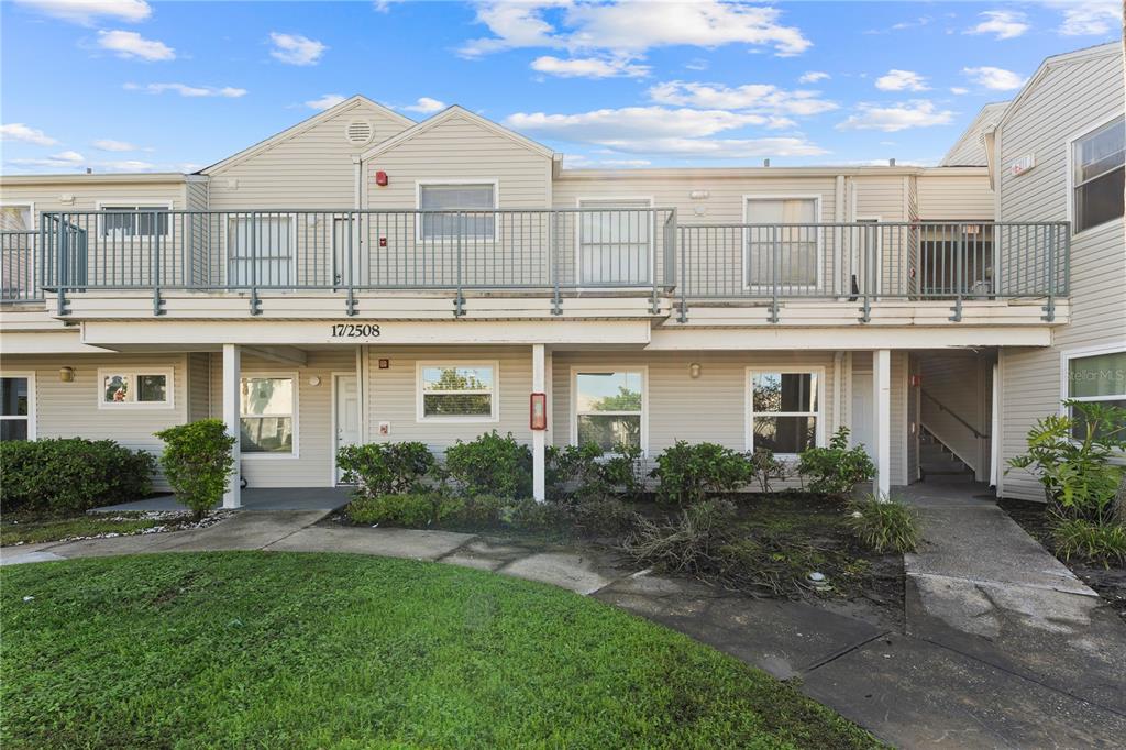 A two-story apartment building with light-colored siding, a balcony, and a concrete walkway — 2508 WOODGATE BOULEVARD UNIT 105, ORLANDO, FL