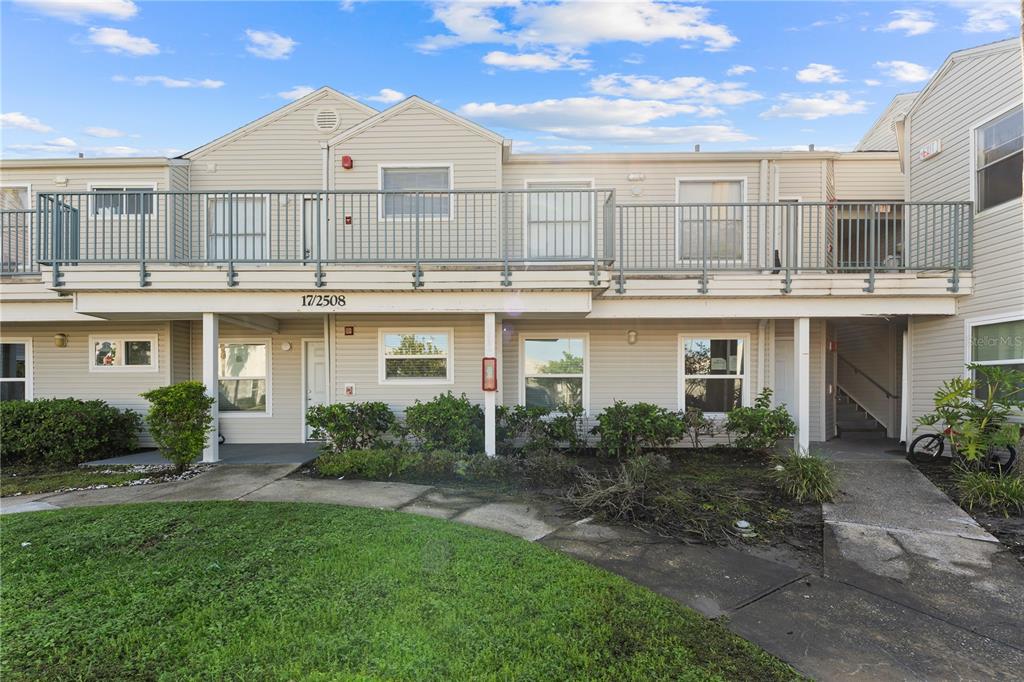 A two-story apartment building with light-colored siding, a balcony, and a concrete walkway — 2508 WOODGATE BOULEVARD UNIT 105, ORLANDO, FL
