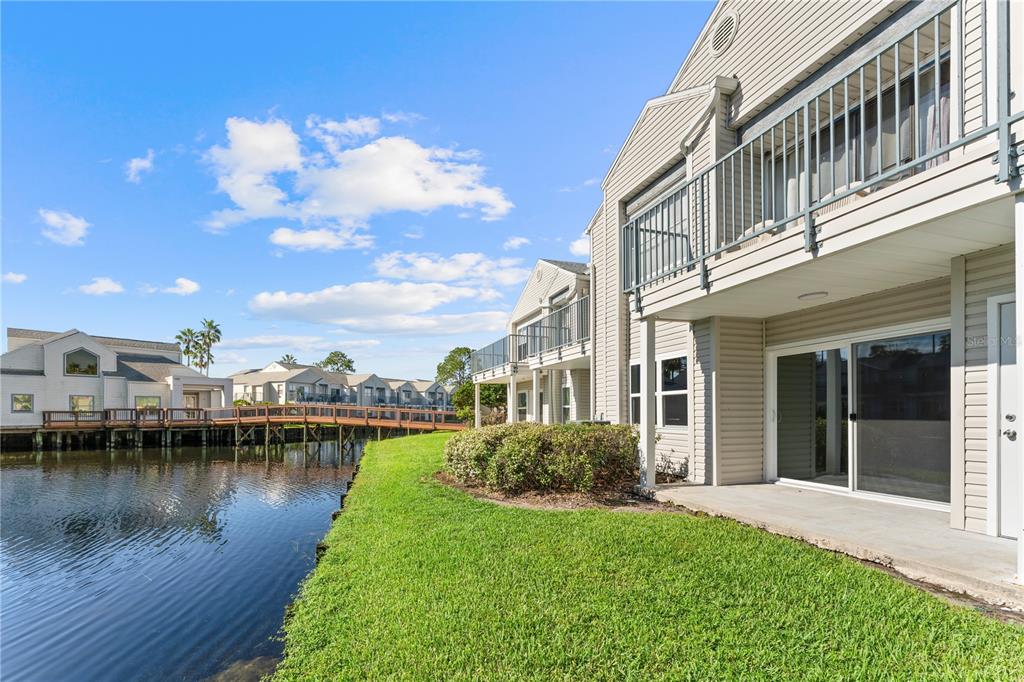 A view of a multi-story apartment building with a patio, lawn, and a wooden bridge — 2508 WOODGATE BOULEVARD UNIT 105, ORLANDO, FL