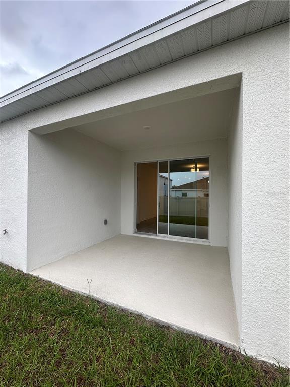 A covered concrete patio sits outside a sliding glass door on a white stucco home — 1623 MARKSMAN ROAD, EAGLE LAKE, FL