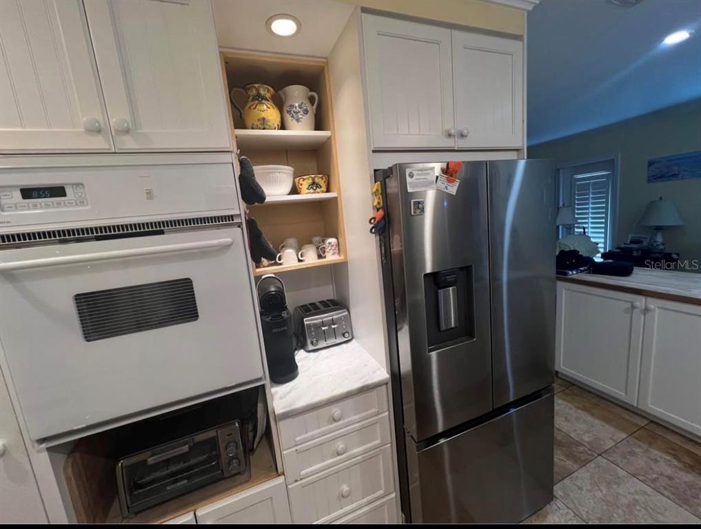 A kitchen features white cabinets, a black cooktop, stainless steel appliances, and a marble countertop — 5164 BEACH DRIVE SE UNIT B furnished, ST PETERSBURG, FL