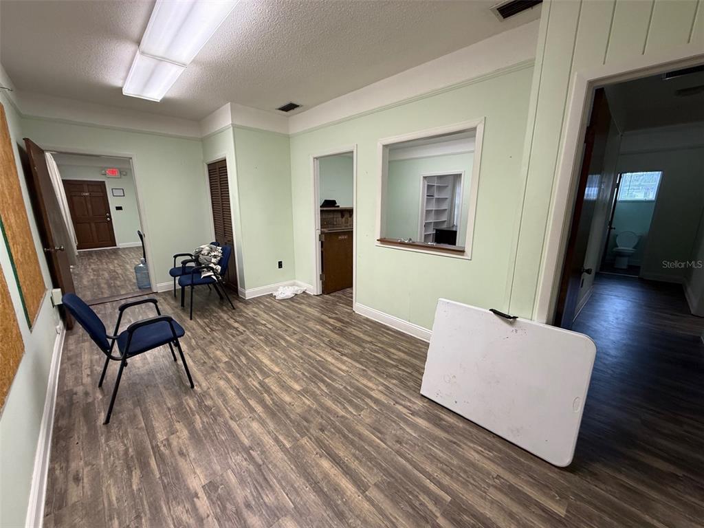 A waiting room with light green walls, wood-look flooring, two blue chairs, and a pass-through window — 818 E SILVER SPRINGS BOULEVARD, OCALA, FL