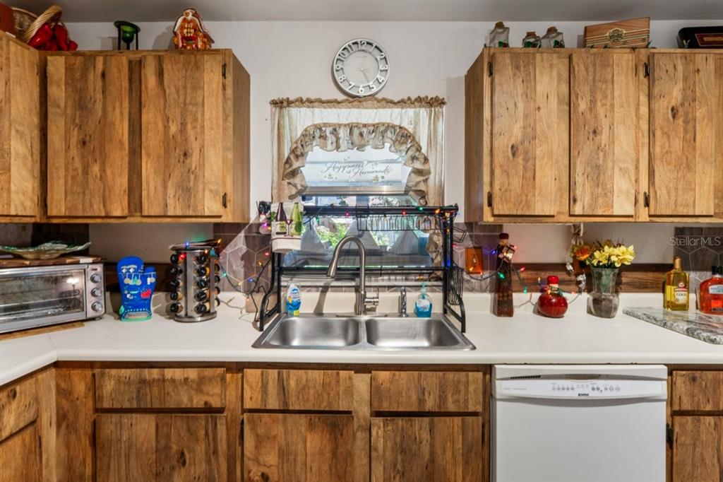A kitchen features wood-grain cabinets, a double-basin sink, white countertops, and a window with curtains — 2005 HUDSON CT, OLDSMAR, FL