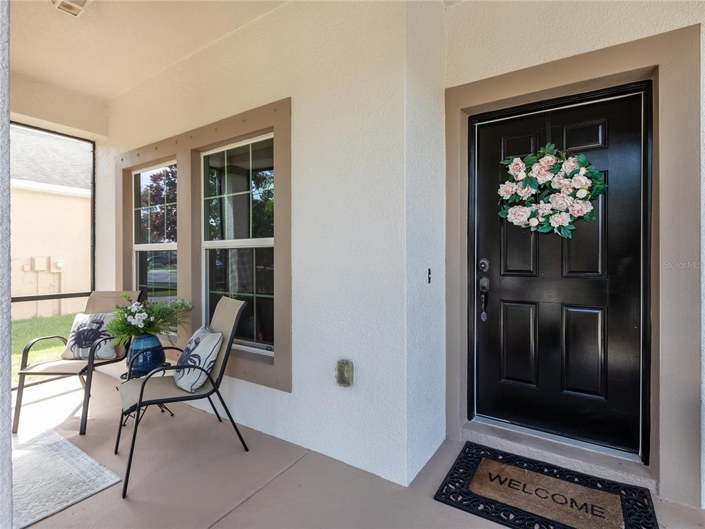 A covered front porch features two chairs, a black door with a wreath, and a mat — 11323 80TH STREET E, PARRISH, FL