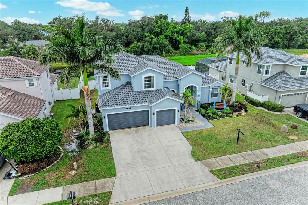 An aerial view of a two-story blue suburban house with a three-car garage and palm trees — 1656 PINYON PINE DR, SARASOTA, FL