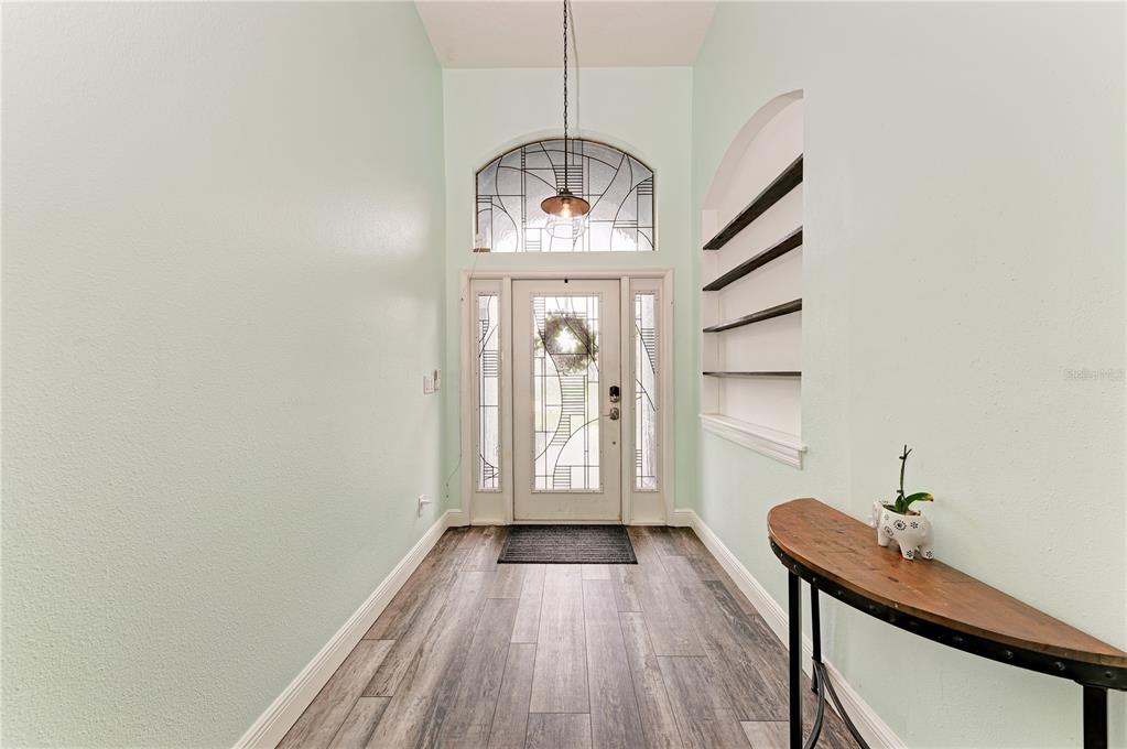 A bright entryway features light green walls, wood-look flooring, a glass-paneled door, and built-in shelving — 1656 PINYON PINE DR, SARASOTA, FL