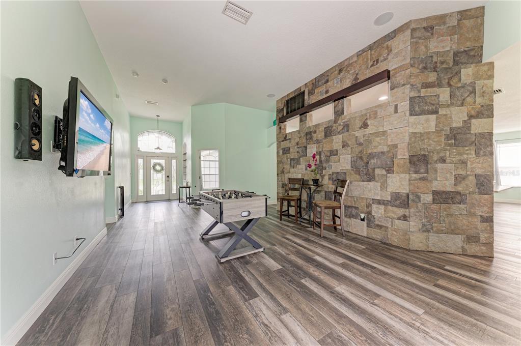 A room with wood-look flooring, a stone accent wall, a foosball table, and a wall-mounted television — 1656 PINYON PINE DR, SARASOTA, FL