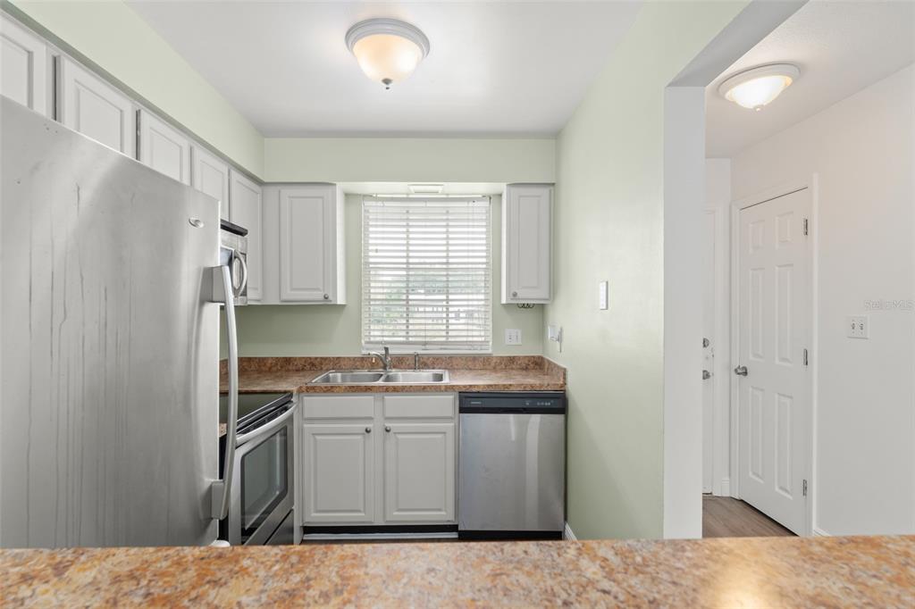 A kitchen features white cabinets, stainless steel appliances, a double sink, and light green walls — 1250 S DENNING DR Unit 233, WINTER PARK, FL