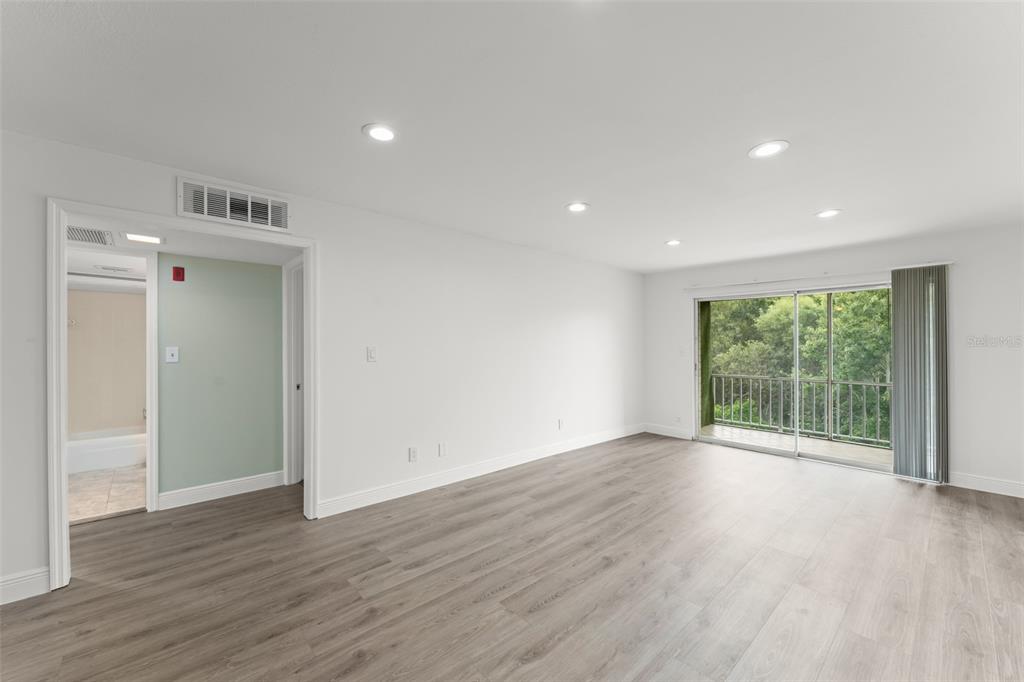 An empty room with light wood-look flooring, recessed lighting, and a sliding glass balcony door — 1250 S DENNING DR Unit 233, WINTER PARK, FL