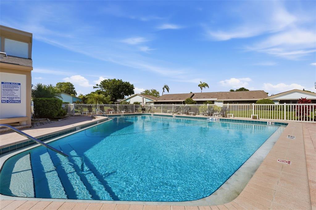 A white stucco house exterior features a dark-framed storm door and a landscaped garden bed — 6132 29TH AVENUE W UNIT 6132, BRADENTON, FL