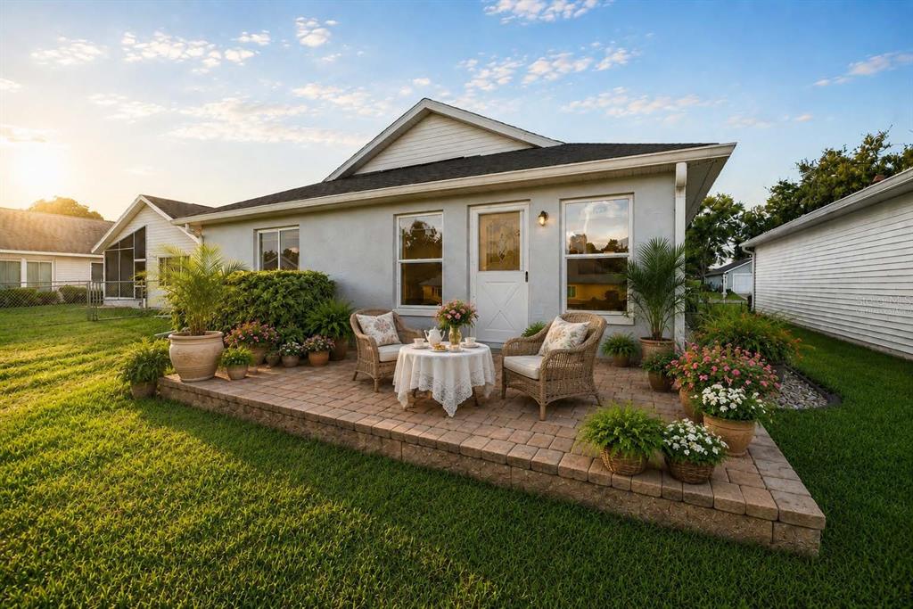 A paved patio with wicker chairs and a small table sits behind a suburban house — 1923 NW 50TH CIRCLE, OCALA, FL