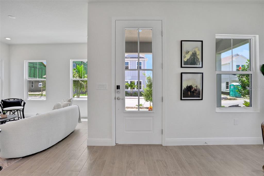 A bright living area features light wood flooring, a white sofa, and a glass-paneled door — 9135 WALCOTT LANE, LAKEWOOD RANCH, FL