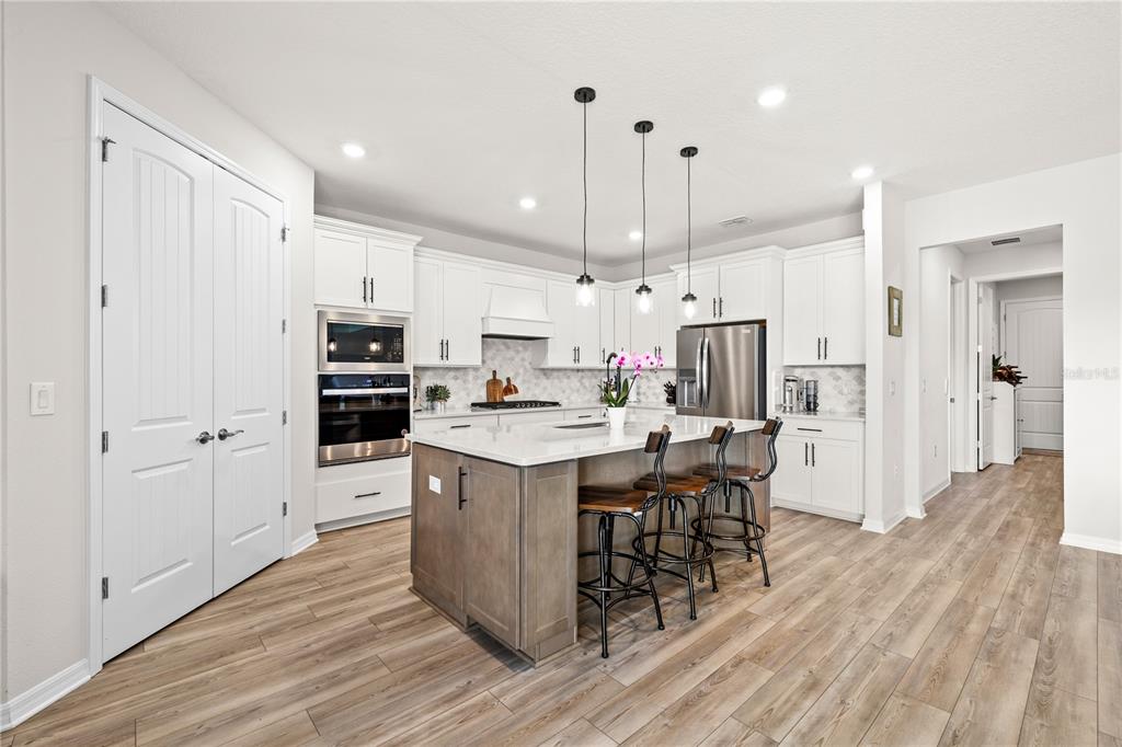 A modern kitchen features white cabinets, a wood-toned island with bar seating, and stainless appliances — 5269 FOOTHILLS PRESERVE LOOP, MOUNT DORA, FL