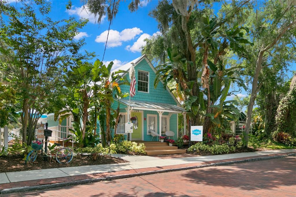 A turquoise cottage with a front porch, American flag, and lush landscaping on a brick street — 135 4TH AVENUE N, SAFETY HARBOR, FL