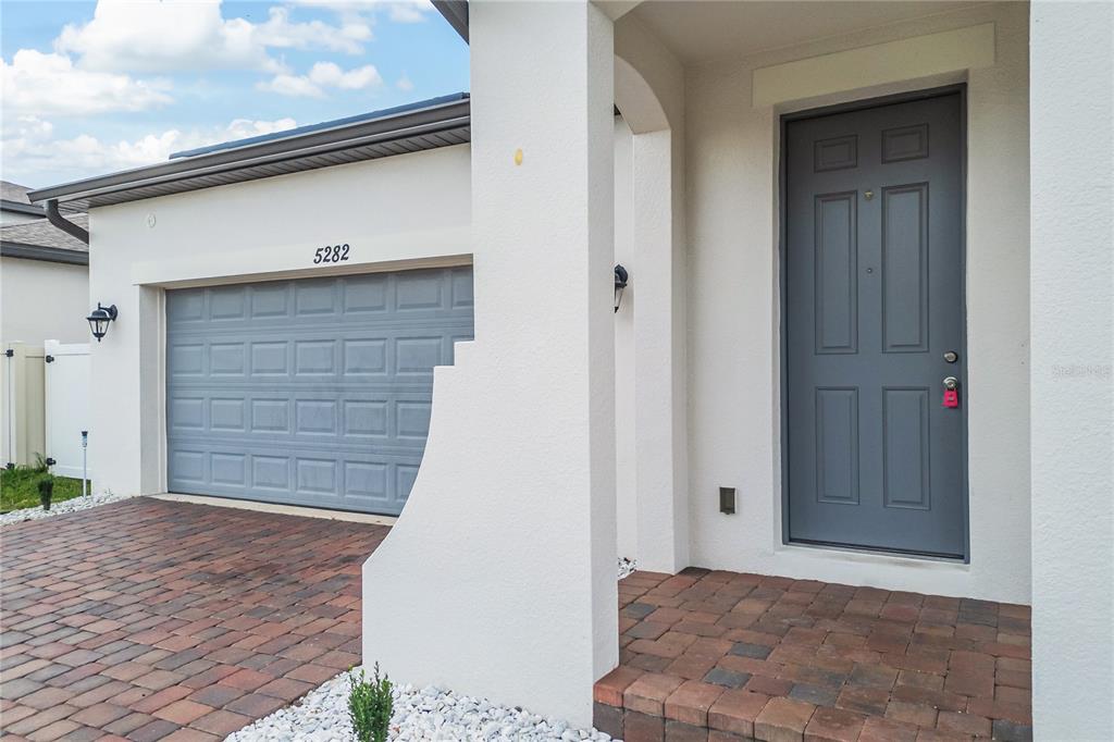 A house exterior features a gray garage door, a matching front door, and brick pavers — 5282 PAVIA DRIVE, ST CLOUD, FL