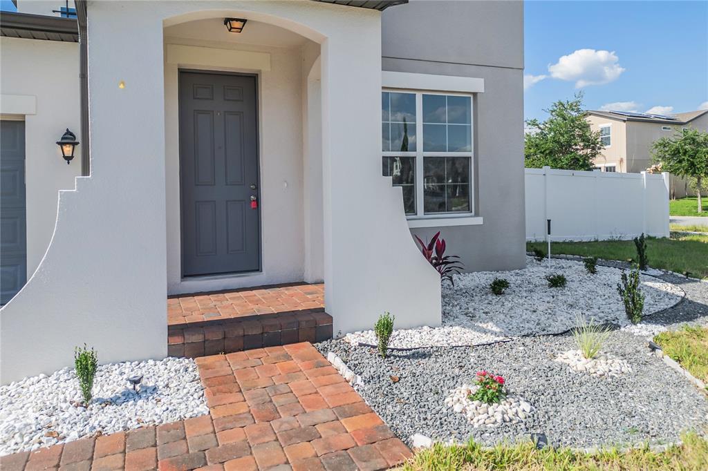 A gray front door is set within a white arched entryway with a brick walkway — 5282 PAVIA DRIVE, ST CLOUD, FL
