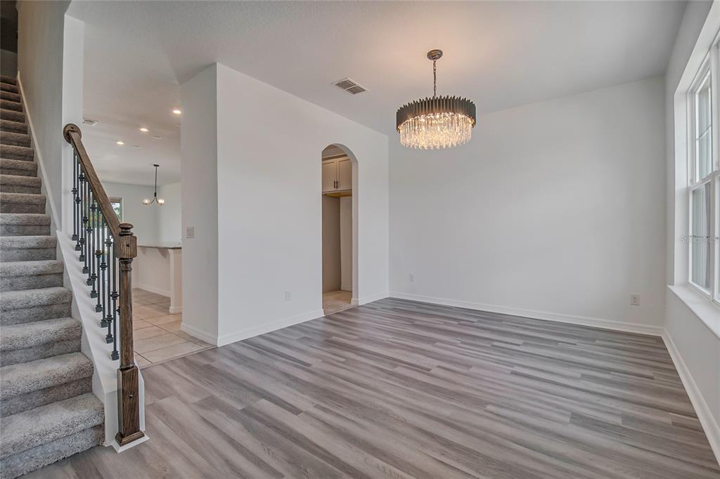 A dining room with gray wood-look flooring, a crystal chandelier, and a staircase — 5282 PAVIA DRIVE, ST CLOUD, FL