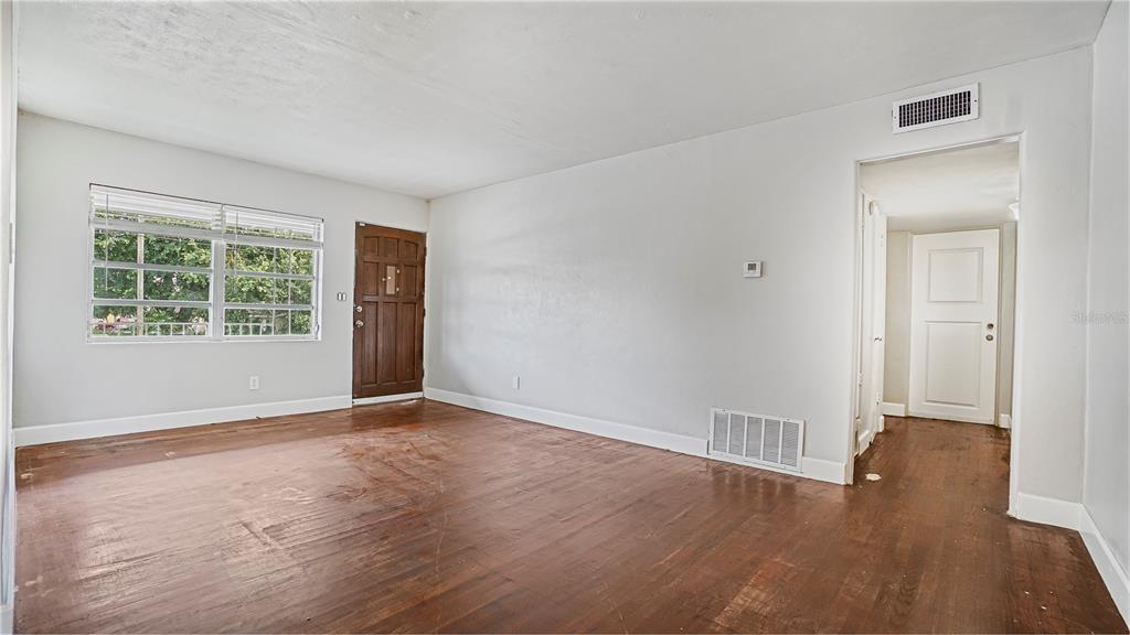 An empty room with hardwood floors, a wooden front door, and a white interior door — 5518 RIVIERA DRIVE, ORLANDO, FL