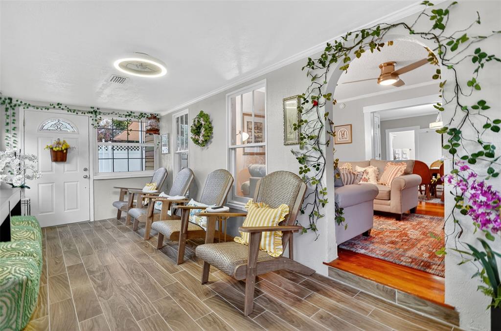 A sunroom with wood-look tile floors features three wicker chairs and an arched entryway — 418 E 10TH AVENUE, MOUNT DORA, FL