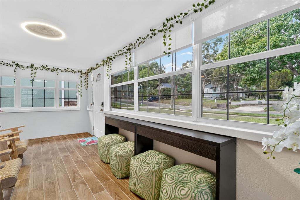A sunroom features wood-look tile flooring, large windows, a long console table, and green ottomans — 418 E 10TH AVENUE, MOUNT DORA, FL