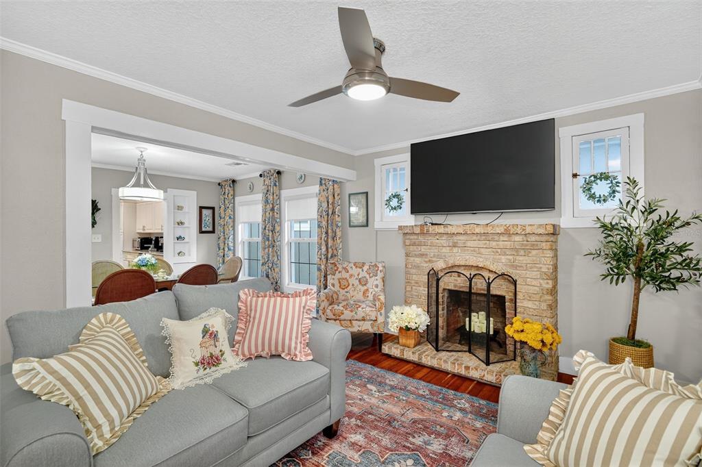 A living room features a brick fireplace, a television, a ceiling fan, and gray furniture — 418 E 10TH AVENUE, MOUNT DORA, FL