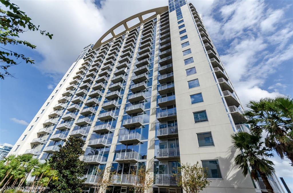 A low-angle view of a tall, modern residential high-rise building with many glass balconies — 155 S COURT AVENUE UNIT 2705, ORLANDO, FL
