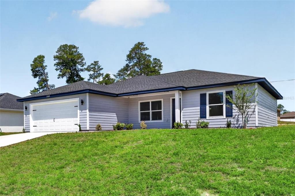A single-story house with gray siding, a white garage door, and a surrounding wooded area — 24303 SW SAILBOAT DRIVE, DUNNELLON, FL