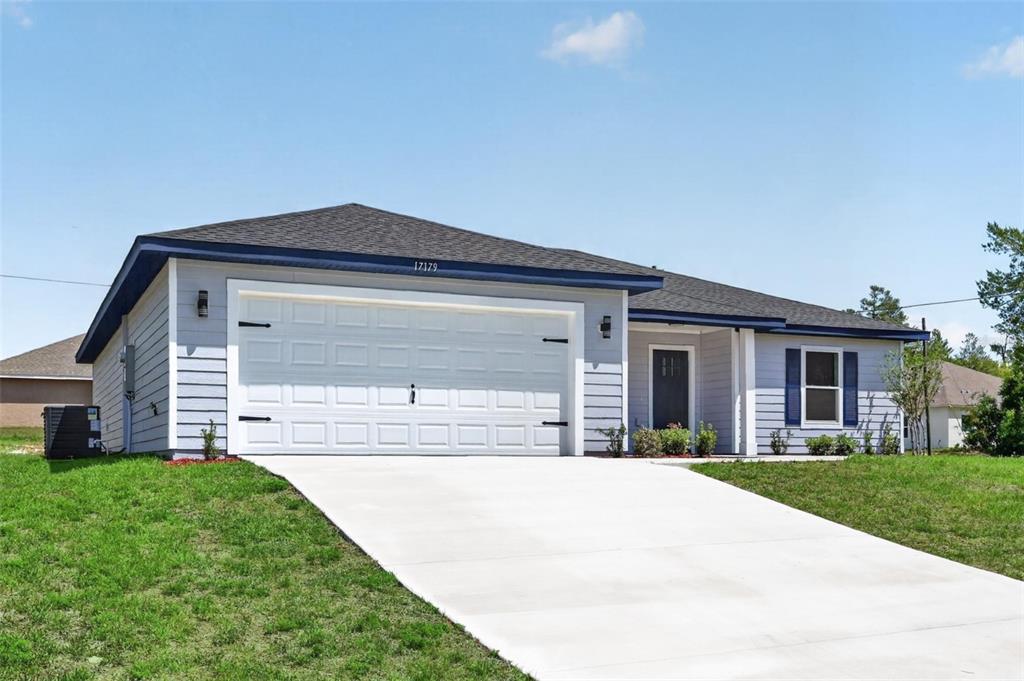A gray house exterior features a blue front door, a covered porch, and landscaping — 24303 SW SAILBOAT DRIVE, DUNNELLON, FL